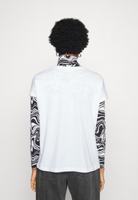 Camiseta blanca de manga corta con mangas largas de mármol en blanco y negro, con un cuello redondo y corte relajado, combinada con pantalones grises.