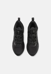 Des chaussures de sport noires avec un dessus en maille texturée, une semelle en caoutchouc épaisse et un système de laçage rapide. Dotées d'une languette au talon et d'accents réfléchissants.