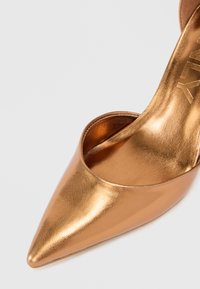 Brončana pumpa s oštrim vrhom izrađena od metalik kože, s elegantnim dizajnom, otvorenim leđima i glatkom teksturom.