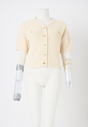 Knit cream cardigan with short sleeves, featuring a v-neck, textured fabric, gold buttons, and two chest pockets on a mannequin.