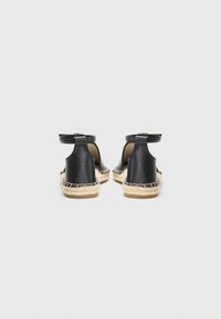 Mustad nahast espadrillid, millel on põimitud jute põhi, avatud seljaosa disain, pahkluu rihm ja dekoratiivne tikand äärtes.