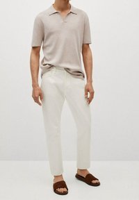 Polo shirt beige clair à manches courtes, pantalon blanc à jambe droite et sandales à glissière marron. Texture lisse et design classique de col.