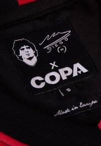 Zwarte stoffen label met witte tekst, met een portret, een handtekening en de tekst "COPA x DIEGO" en "Made in Europe."