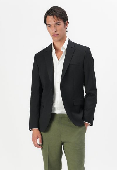 Blazer noir avec revers à cran, fermeture à un bouton et poche avant, associé à une chemise blanche et un pantalon vert. Texture de tissu lisse.