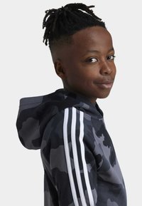 Hoodie in camouflage nero e grigio con strisce bianche sulle maniche, realizzato in un tessuto morbido e con una vestibilità comoda. Cappuccio integrato per un look casual.