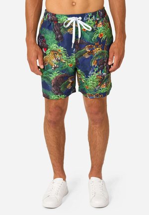 Herenshorts met een jungledessin met gorilla's, luipaarden en groene bladeren, gecombineerd met witte sneakers en een witte tailleband met trekkoord.