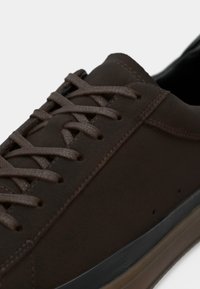 Bruna lädersneakers med en slät yta, tunna snören och en gummisula med en subtil, lagerdesign.