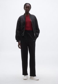 Czarna kurtka bomberka na czerwonej koszuli, w połączeniu z czarnymi dresami i białymi trampkami. Kurtka posiada zamek błyskawiczny i elastyczne mankiety.