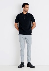 Polo negro de manga corta con cuello de cremallera, combinado con pantalones ajustados de color gris claro y botas negras de tobillo. Textura suave y diseño minimalista.