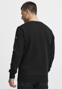 Zwarte sweatshirt met een gestructureerde afwerking, ronde halslijn, ribgebreide manchetten en tailleband. Bevat een klein label op de linkermouw.
