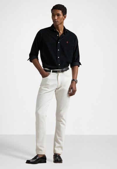 Black button-up shirt, white slim-fit pants, black belt, and black slip-on shoes. Shirt features a small logo; smooth fabric texture.
