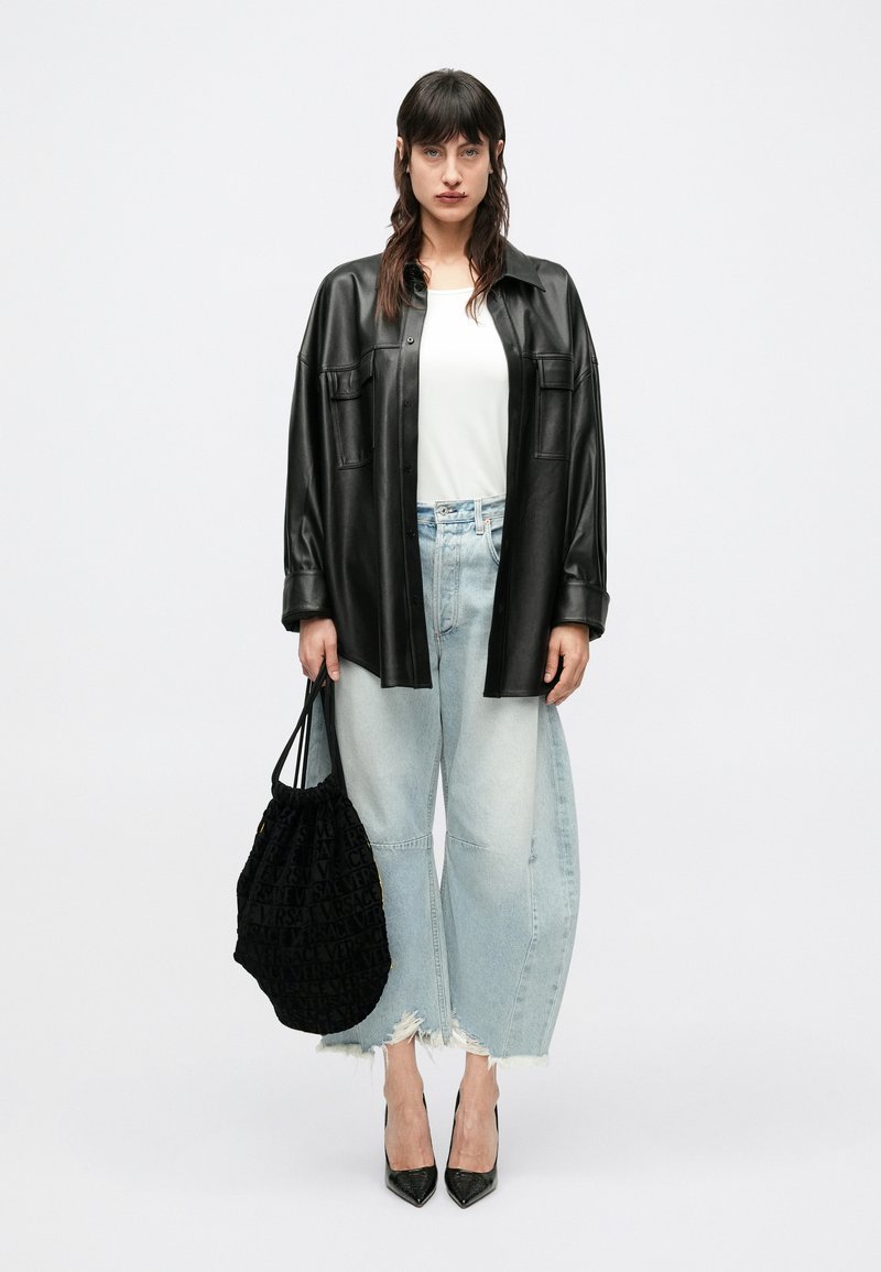 Sort læder oversize skjorte, hvid t-shirt, lyseblå vidde-bukser med frynsede kanter og sort logo taske. Sorte høje hæle fuldender looket.