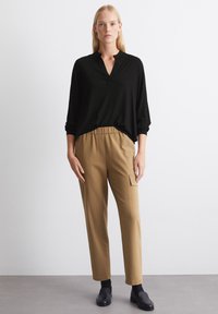 Blusa nera a maniche lunghe con scollo a V e vestibilità ampia, abbinata a pantaloni marroni a sigaretta con tasca laterale e vita elasticizzata.