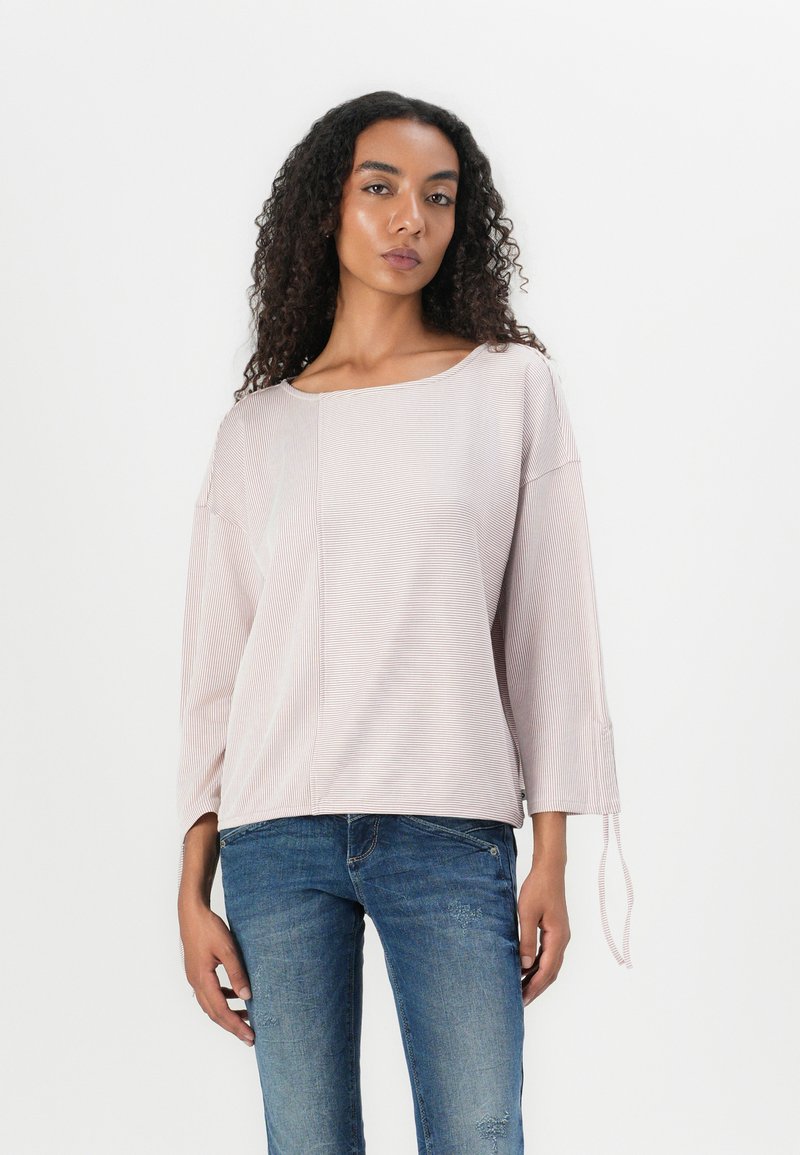Lys rosa stripete langermet topp med båthals, løs passform og knytedetalj på ermene, kombinert med blå slitte jeans.