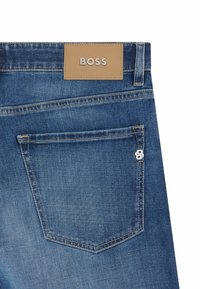 Blue denim jeans with a brown leather tag marked "BOSS." Features a back pocket with contrasting stitching and a small silver hardware accent.
