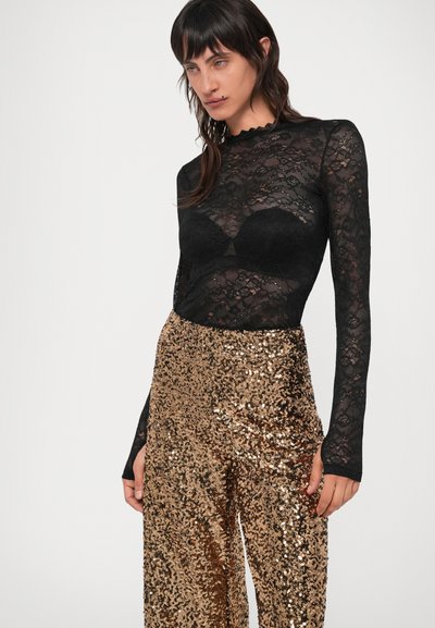 Top de encaje negro de manga larga con escote festoneado, combinado con pantalones ajustados de cintura alta y lentejuelas doradas brillantes. Diseño texturizado y ceñido.