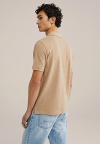 Camisa polo beige hecha de tela suave, con cuello y mangas cortas. Combinada con jeans de mezclilla azul claro, que presentan una abertura lateral en el dobladillo.