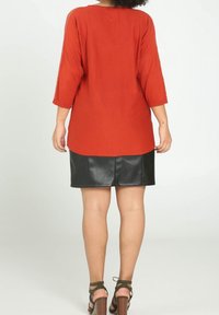 Rood, loszittend bovenstuk met driekwart mouwen, gecombineerd met een zwarte leren mini-rok en bruine sandalen met bandjes. Gladde textuur, casual ontwerp.