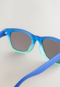Occhiali da sole blu con un bordo interno verde sfumato, lenti grigie e una finitura liscia opaca. Presentano una montatura rotonda e bracci eleganti.