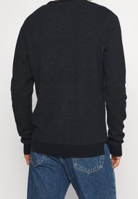 Dunkelblaues Sweatshirt mit strukturiertem Design, Rundhalsausschnitt und engen Bündchen; kombiniert mit hellblauen Jeans.