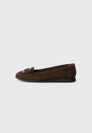 Chaussure plate en daim marron avec semelle noire et boucle décorative sur le dessus, montrée de profil sur un fond gris clair uni.