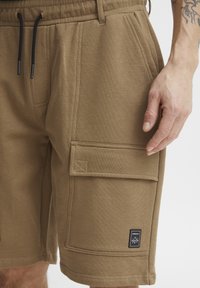 Cargo-Shorts aus Baumwollmischung in Braun, mit elastischem Bund, Seitentaschen und einem quadratischen Logo-Patch auf dem Oberschenkel.