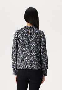 Blusa floreale con sfondo nero, piccoli fiori blu e verdi, scollatura alta, dettaglio con apertura a chiave sul retro e maniche lunghe a sbuffo.