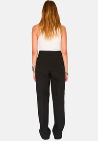 Pantalons noirs ajustés avec un design à jambes droites, comportant deux poches arrière et une texture lisse. Portés avec un débardeur blanc.