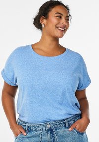 Hellblaues T-Shirt mit kurzen Ärmeln, rundem Ausschnitt und umgekrempelten Bündchen, aus strukturiertem Stoff. Kombiniert mit hoch tailliertem Denim.