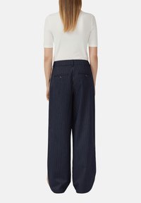 Marineblauwe pinstripe wijde broek met een hoge tailleband, voorzien van twee achterzakken en een gladde textuur. Gestyled met een aansluitend wit topje.