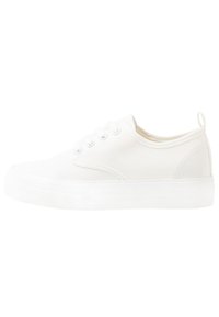 Sneaker di tela bianca con punta rotonda, dettagli di cucitura visibili, design con lacci e suola in gomma trasparente.