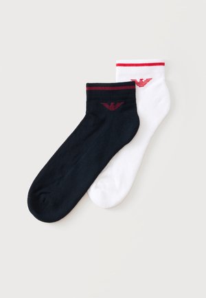 Paire de chaussettes basses, une noire et une blanche, chacune avec un logo rouge et une bande rouge près du bord-côte, présentées sur un fond plat clair.