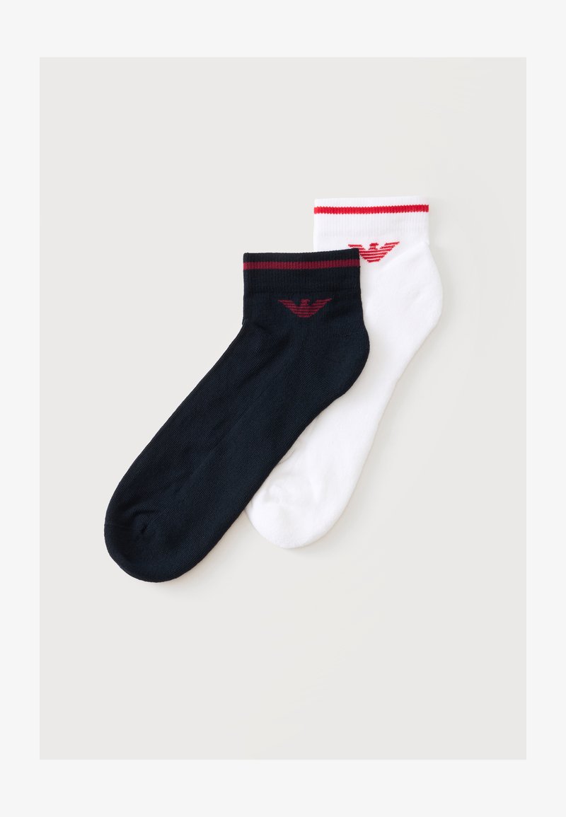 Paire de chaussettes basses, une noire et une blanche, chacune avec un logo rouge et une bande rouge près du bord-côte, présentées sur un fond plat clair.