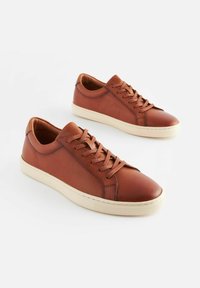 Bruna lädersneakers med en texturerad yta, platta snören och en krämfärgad gummisula. Har en strömlinjeformad design för avslappnad användning.