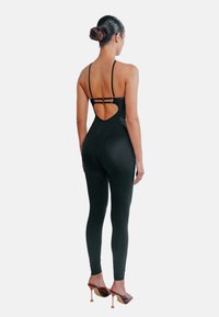 Svart, figurnära jumpsuit med spaghettiband, en hjärtformad uringning baktill och bronsfärgade metalldetaljer. Bärs med klackade sandaler.