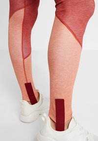 Leggings de sport rouges et pêche avec une finition texturée, présentant des blocs de couleur diagonaux et un accent rouge contrastant à la cheville.
