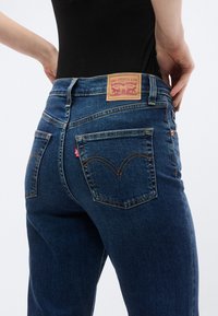 Σκούρο μπλε τζιν με καφέ δερμάτινο ταμπελάκι με κόκκινα γράμματα, δύο πίσω τσέπες και χαρακτηριστικό ραφικό σχέδιο.