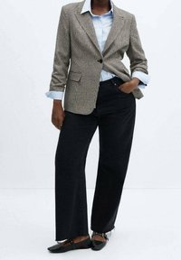 Hnědý sako s vzorem jelení tlapky na jednobtné zapínání, v kombinaci s světle modrou košilí s límečkem a černými širokými džínami. Černé baleríny doplňují outfit.