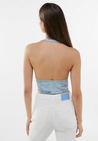 Svetle modrý denimový halter crop top s bezzadním designem a kovovými druky. V kombinaci s bílými vysokými kalhotami s kapsami na zadní straně.