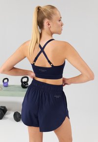 Navy sports bra with cross-back straps and logo; paired with loose navy shorts featuring an elastic waistband and side slits for comfort.