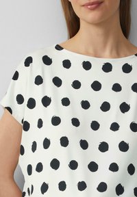Witte korte mouwen top met een zwart stippenpatroon. Glad materiaal met een ronde halslijn en een losse fit.