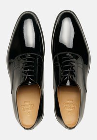 Scarpe oxford in pelle verniciata nera con una finitura liscia e lucida, contrastate da una soletta in pelle color beige chiaro e una dettagliata cucitura lungo i bordi.