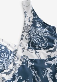 Laivastonsininen ja valkoinen mekko, jossa on kukkakuviota sileässä kankaassa. Suunnittelussa on monimutkaisia yksityiskohtia ja vaihtelevaa tekstuuria.