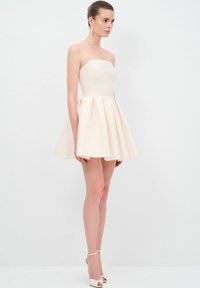 Robe sans bretelles de couleur crème avec un corsage ajusté et une jupe évasée plissée. Texture lisse, longueur genoux avec des embellissements minimaux.