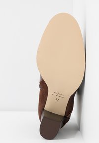 Talons en daim marron avec une semelle beige lisse. Présente un design incurvé et des accents marron foncé. L'étiquette indique la marque "JONAK" et la taille "37".