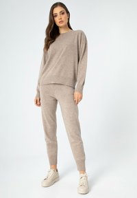 Beiger Strickpullover und passende Jogginghose mit lässiger Passform, langen Ärmeln und Rippbündchen, kombiniert mit hellen Sneakers.