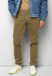 Beige Cordhosen mit schlanker Passform und Fronttasche, kombiniert mit einer blauen Jeansjacke und weißen Sneakers. Einfaches Design, keine Muster.