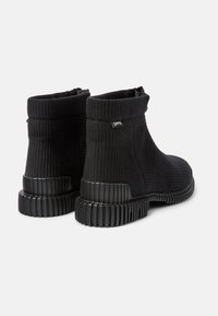 Svarta ankle boots gjorda av ribbat textil med hög krage, som har en tjock ribbad sula och en liten varumärkesetikett på sidan.