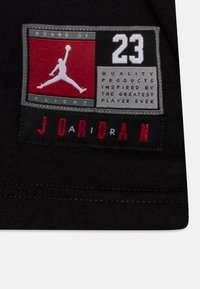 Czarna łatka materiałowa z czerwono-szarym logo, przedstawiająca sylwetkę gracza, tekstem "23" oraz "Marka Lotu" i wyraźnym napisem "JORDAN."