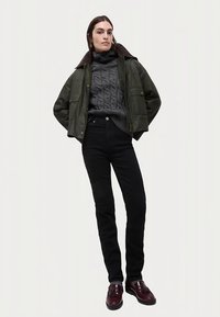 Grön kort jacka med brun krage, grå kabelstickad tröja, svarta smala byxor och vinröda loafers. Avslappnad outfit med lager-på-lager och varierande texturer.